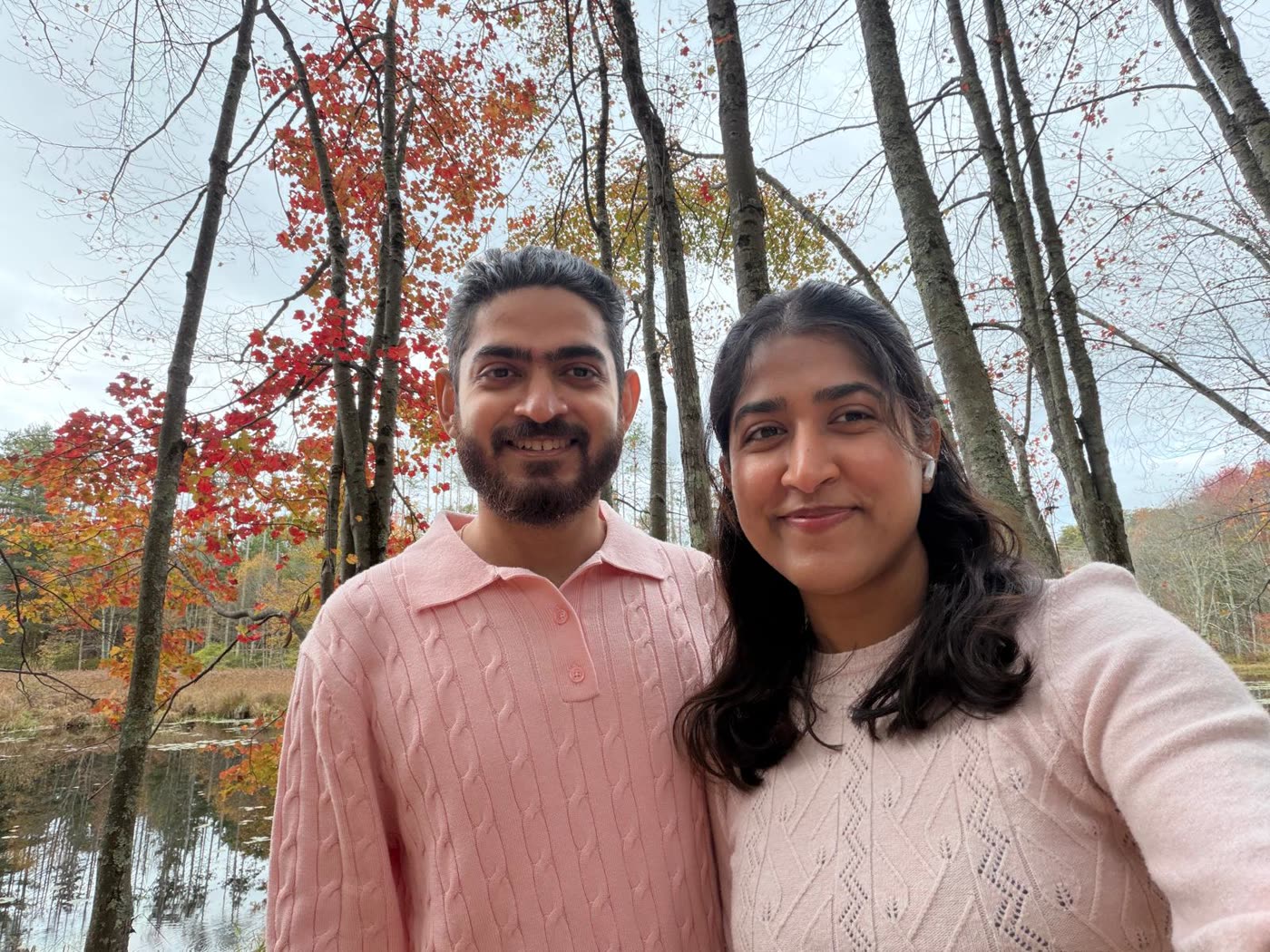 Abirami and Prateek beside a lake ringed with autumn trees